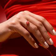 Kenarlarında pırlanta taşları ve ortasında oval kesim yakut taşı bulunan vintage tasarım yüzüğün kırmızı elbise giymiş bir kadın model parmağındaki görüntüsü