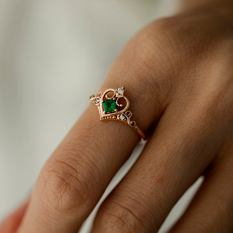 ortasında kare kesim zümrüt taşı ve zümrüt taşının üzerinde ve yanlarında bulunan topam 3 adet küçük pırlanta taşlarıyla tasarlanmış vintage tarzı altın taç yüzüğün kadın modelin parmağındaki görüntüsü 2