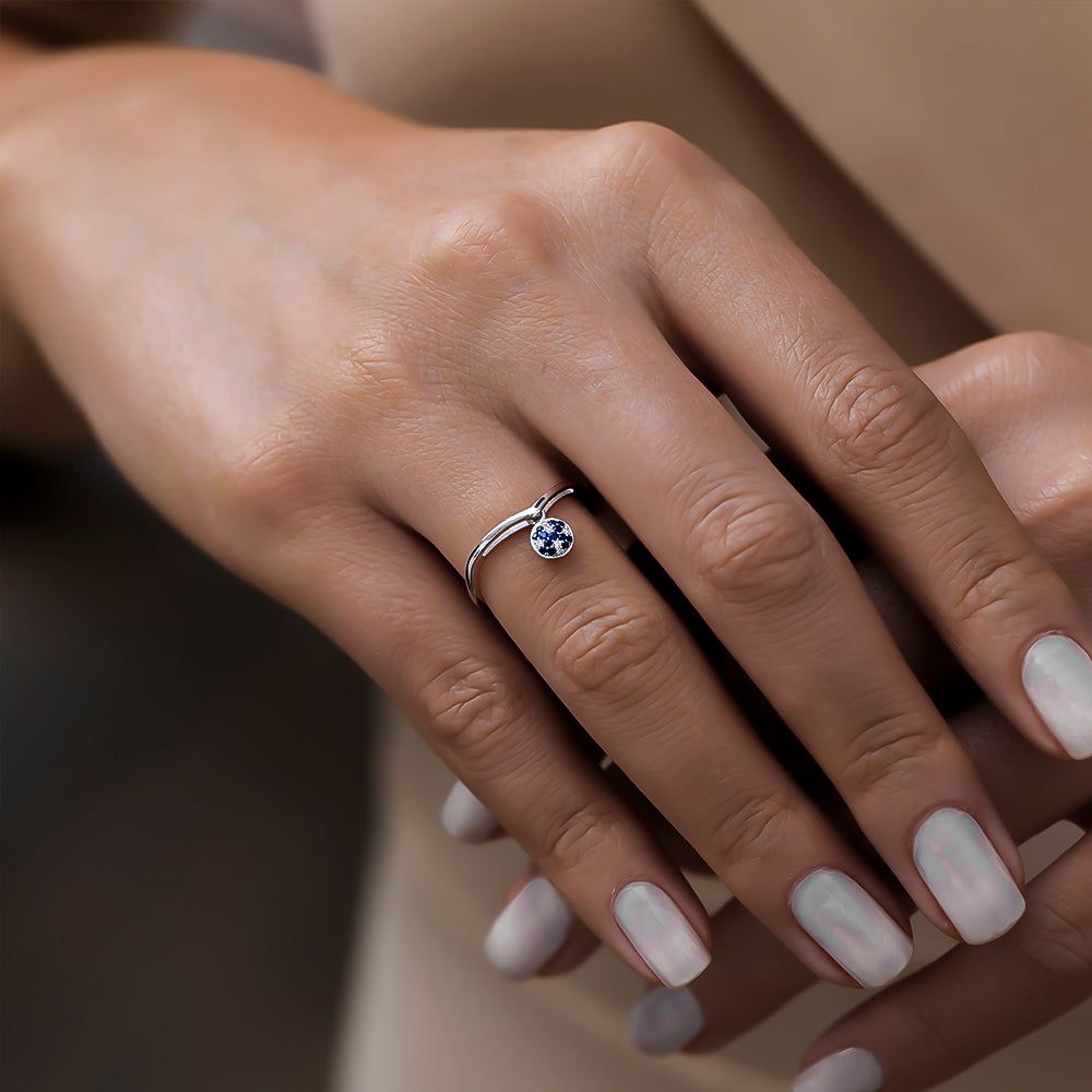 kadın modelin parmağında pırlanta ve safir taşlı sallantılı yüzük